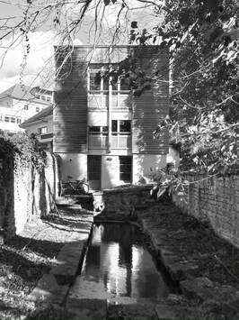 Vue en noir et blanc de l'agence depuis le canal, bâtiment en bois entre les arbres