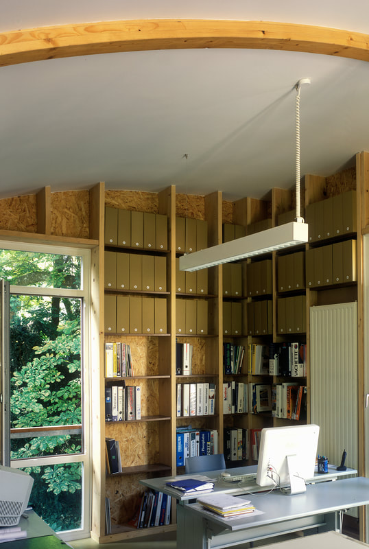 Bibliothèque de l'atelier sous une charpente en bois courbe
