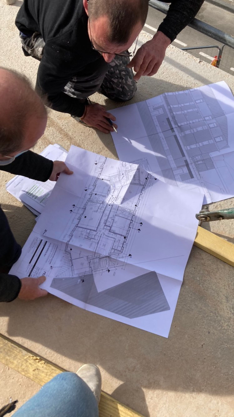 Deux personnes lisent des plans dépliés sur une dalle de chantier