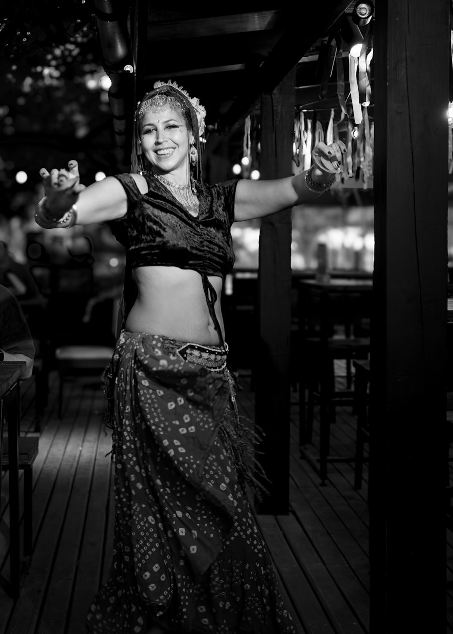 Danseuse orientale souriante en costume brodé, bras ouverts, dans une ambiance chaleureuse