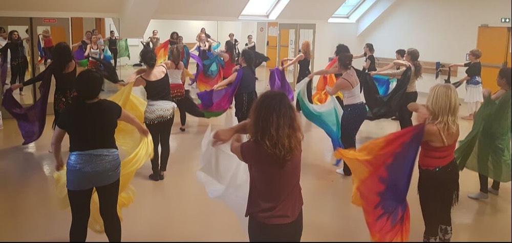 Cours collectif de danse orientale : une vingtaine d'élèves font tournoyer des voiles colorés dans une salle de danse
