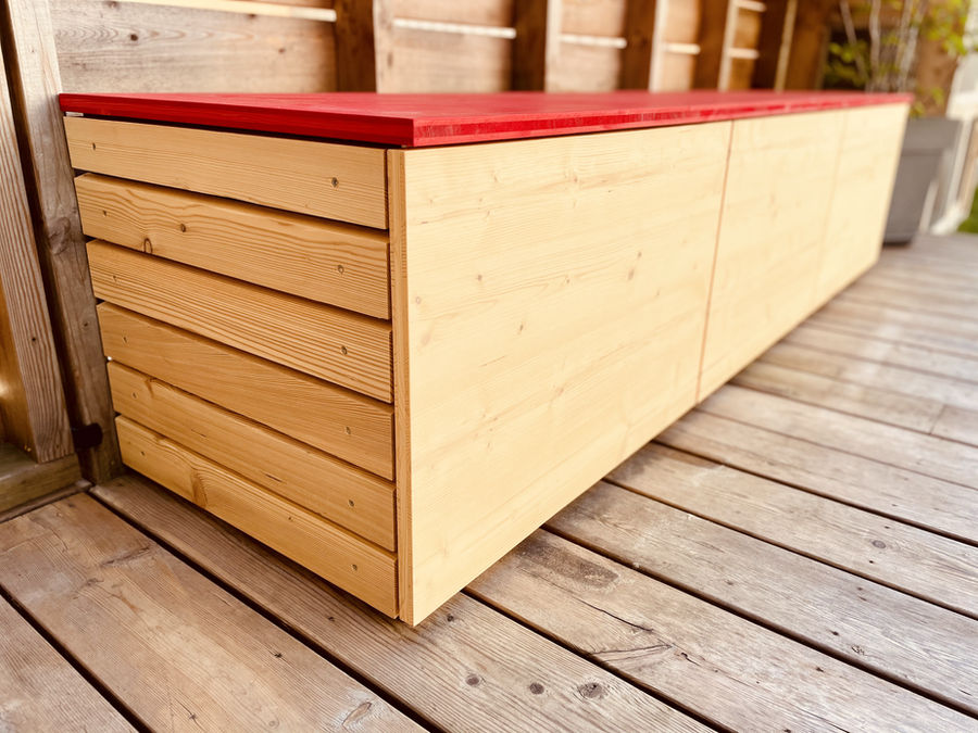 Banc de rangement extérieur en bois avec assise rouge posé sur une terrasse
