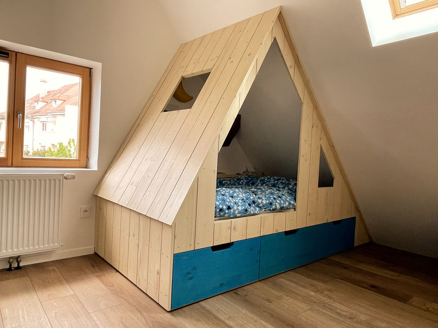 Lit cabane enfant en épicéa avec tiroirs de rangement bleus sous une pente de toit