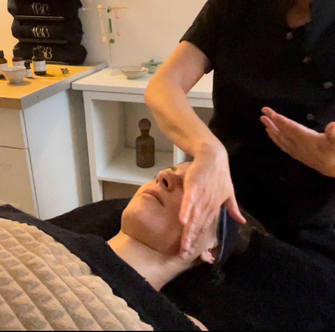 Virginie réalise un massage Kobido du visage avec un gua sha sur une cliente allongée en cabine