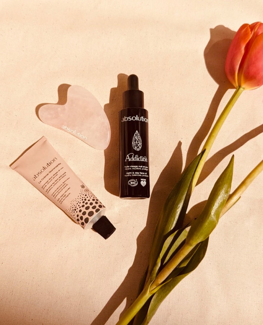 Gua sha en pierre, sérum et crème bio disposés à côté d'une tulipe orange
