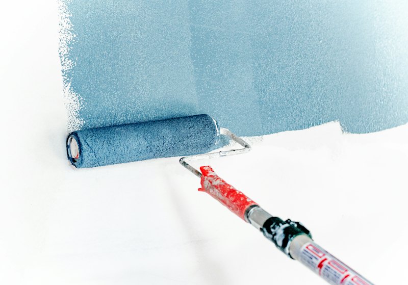 Rouleau appliquant une peinture bleue sur un mur en cours de rénovation.