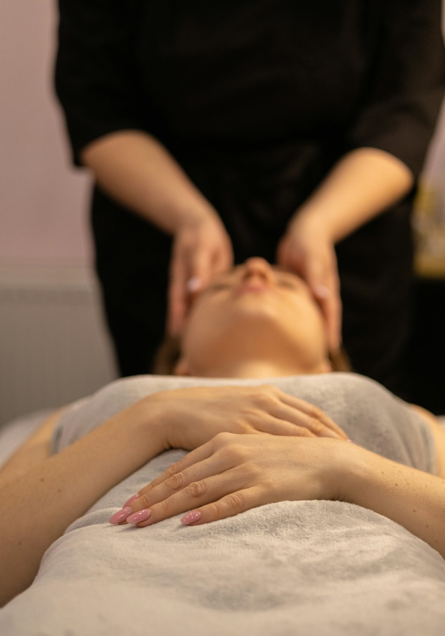 Massage du visage : les mains de la praticienne effleurent les joues d'une cliente aux yeux fermés.