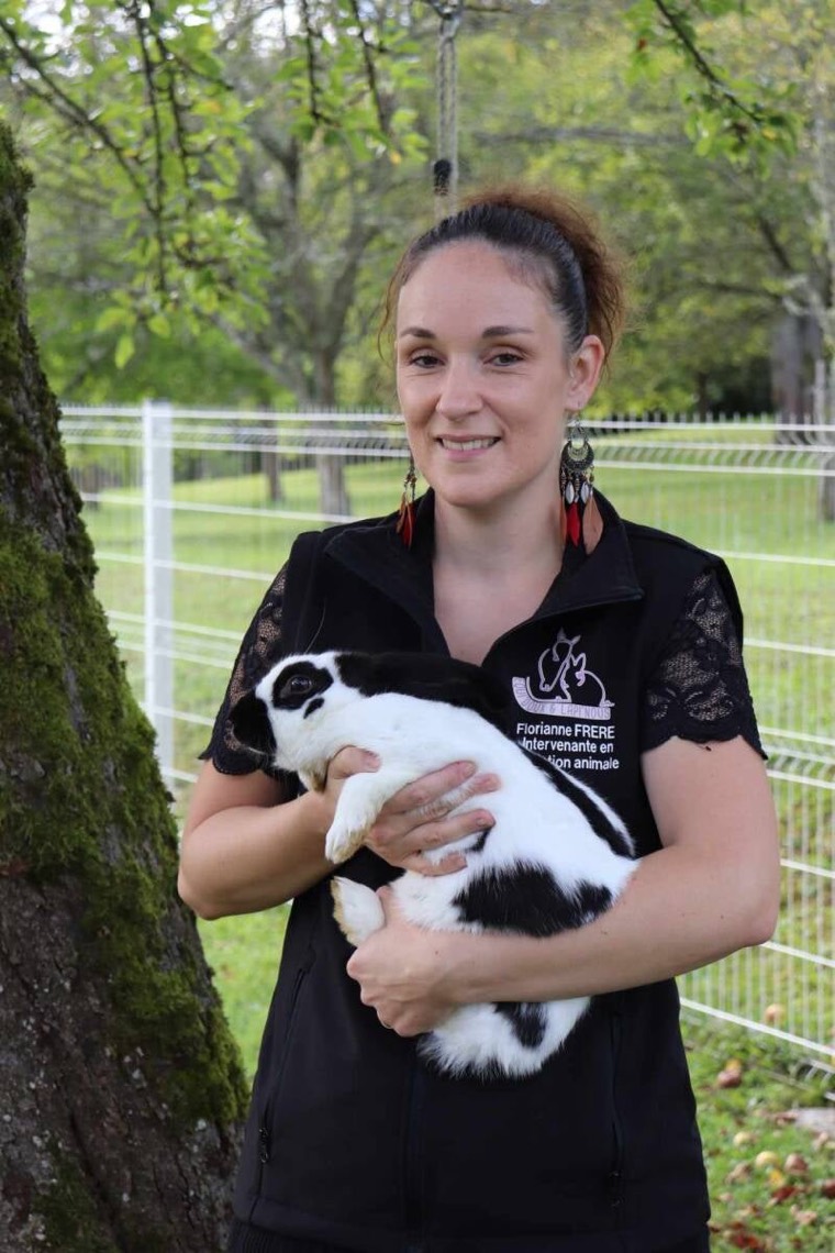 Florianne Frère, intervenante en médiation animale, portant un lapin noir et blanc dans ses bras devant un pré
