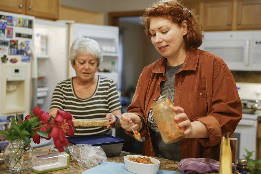 Une aide à domicile prépare un repas en cuisine aux côtés d'une personne âgée