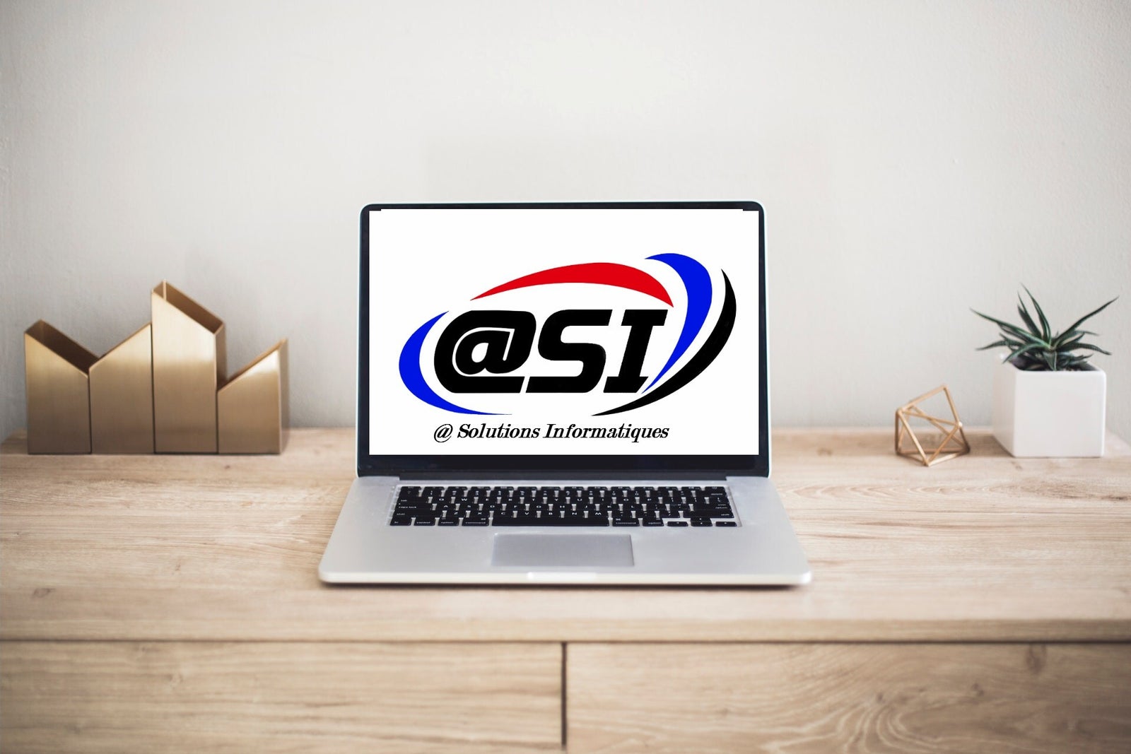 Ordinateur portable affichant le logo @SI, posé sur un bureau en bois clair