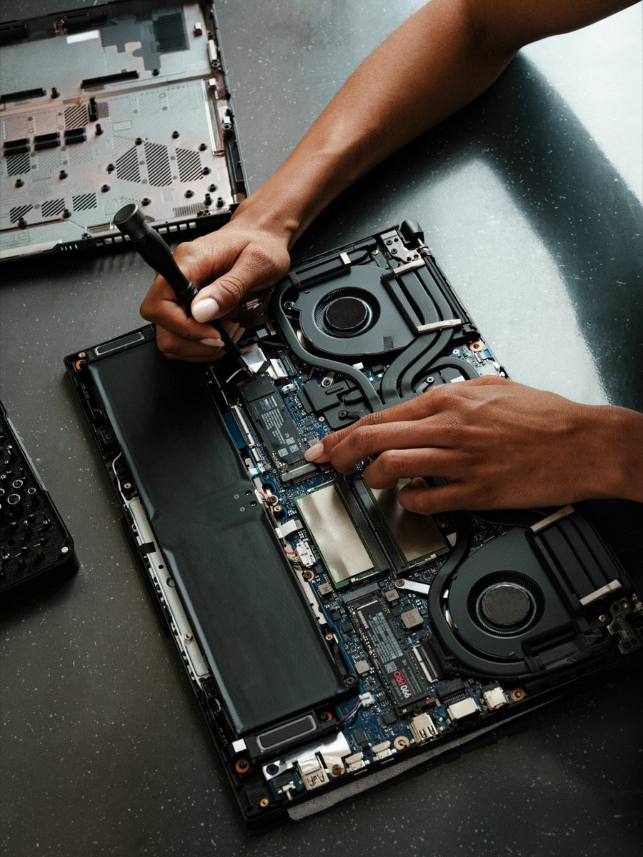 Technicien réparant un ordinateur portable ouvert à l'aide d'un tournevis