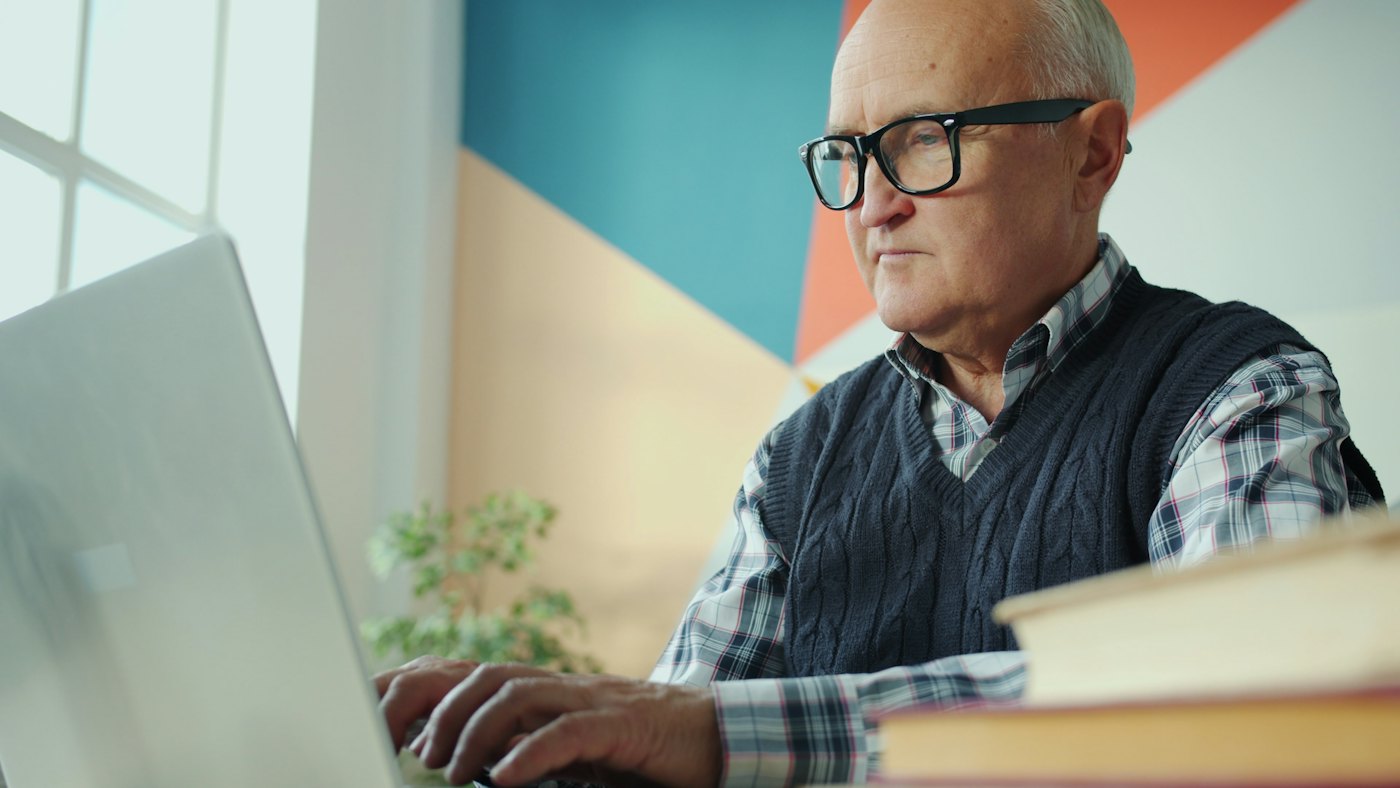 Homme âgé portant des lunettes et utilisant un ordinateur portable chez lui