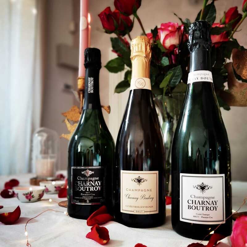 Trois bouteilles de Champagne Charnay Boutroy — Brut Premier Cru, Cuvée Vieilles Vignes et Cuvée Classique — devant un bouquet de roses rouges.