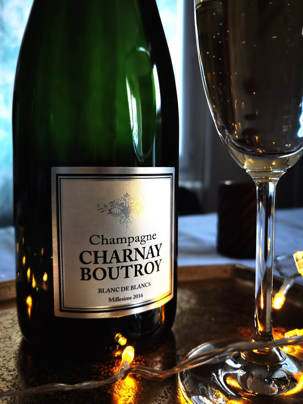 Bouteille de Champagne Charnay Boutroy Blanc de Blancs millésime 2016 et flûte remplie, posées sur un plateau doré.