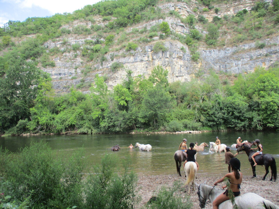 Groupe de cavaliers traversant à cheval une rivière au pied des falaises calcaires du Causse