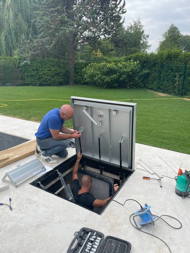 Deux techniciens installant l'automatisme d'une trappe d'accès au local technique d'une piscine