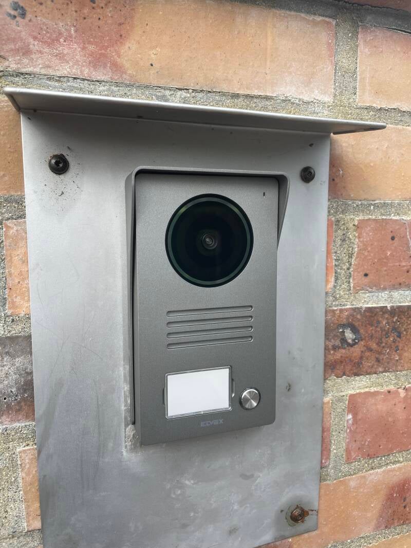 Platine d'interphone avec caméra intégrée fixée sur un mur en brique