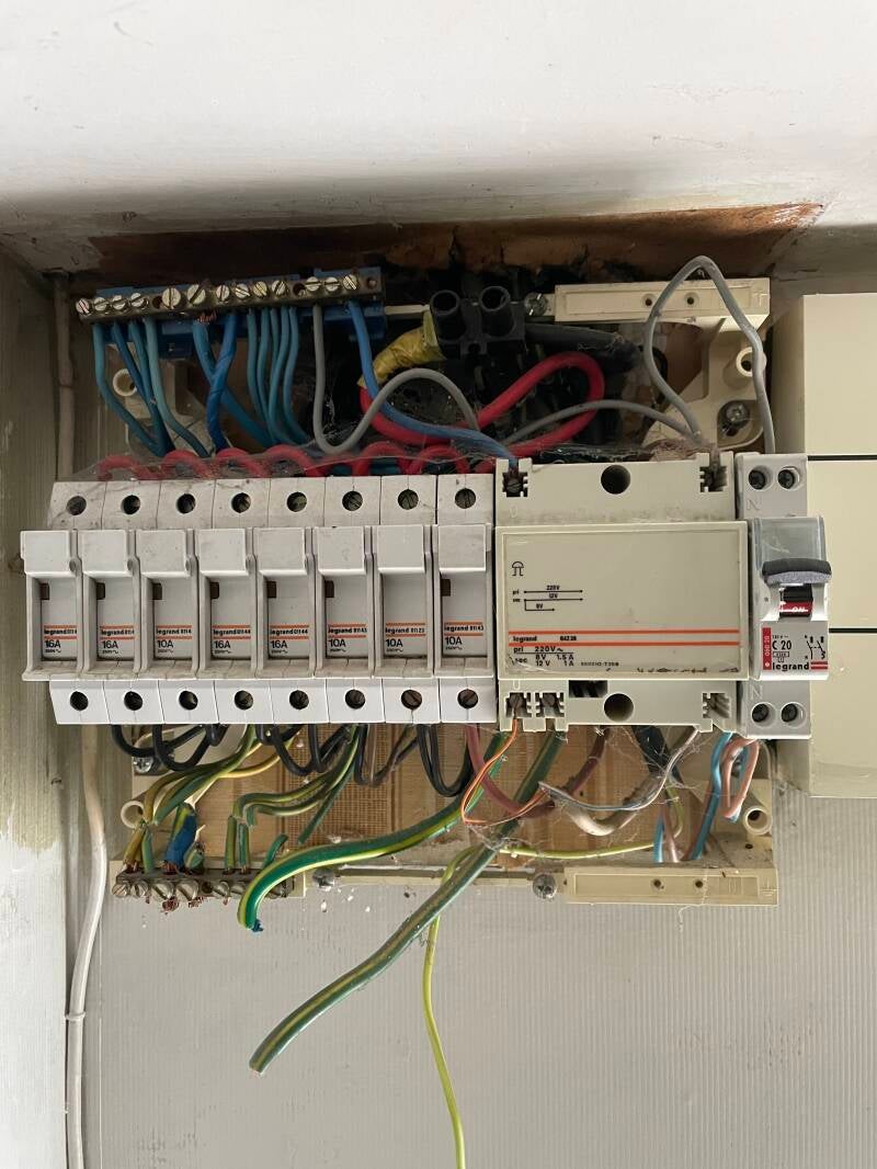 Ancien tableau électrique avant rénovation : câblage apparent et désordonné sur support bois