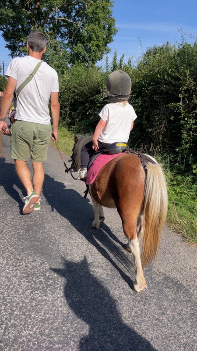 Balade baby : un enfant sur un poney shetland accompagné à pied sur l'allée des écuries