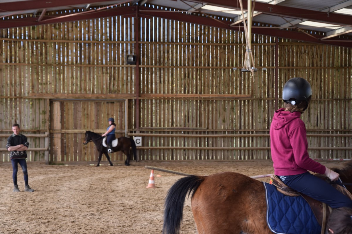 Cours d'équitation dans le manège couvert des Écuries Évasions, une enfant à poney au premier plan