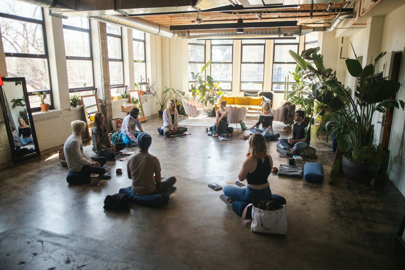 Un groupe de personnes assises en cercle sur le sol d’une pièce lumineuse, lors d’un atelier de relaxation.