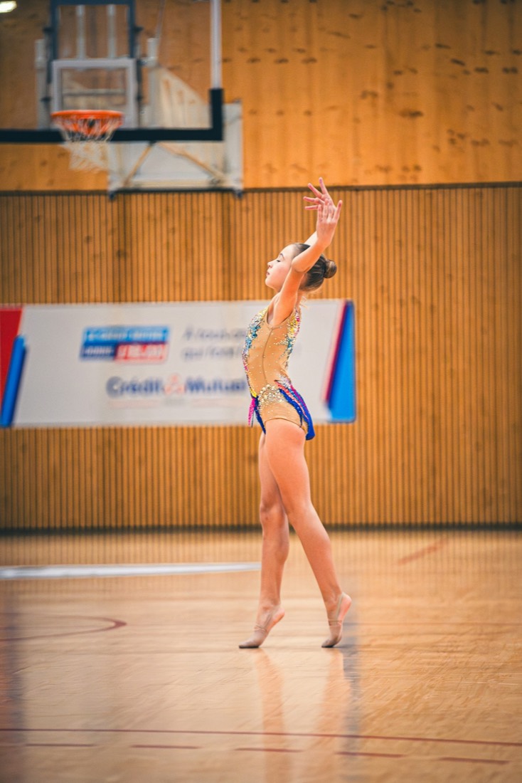 Jeune gymnaste en justaucorps terminant un passage au sol dans un gymnase